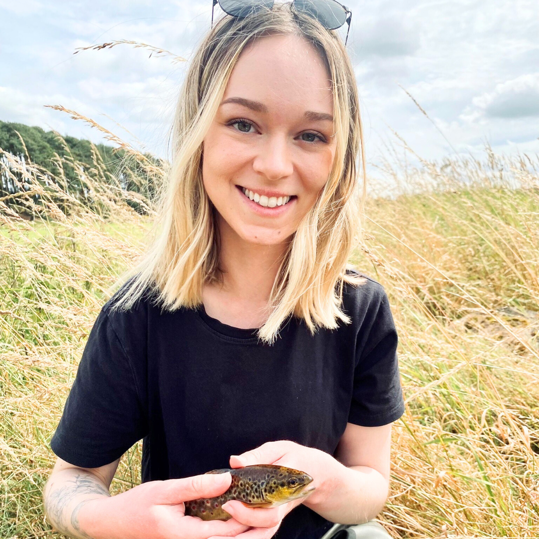 WWT Project Associate Nina Lottsfeldt holds a trout in a grassy field.