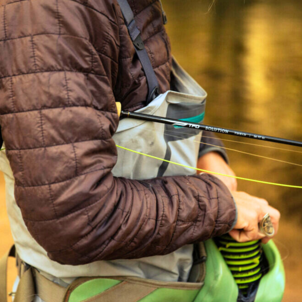 Close up of the arm of a person holding a fly fishing rod.