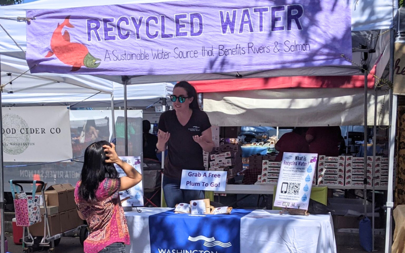 Two people talk at a recycled water booth at a community event.